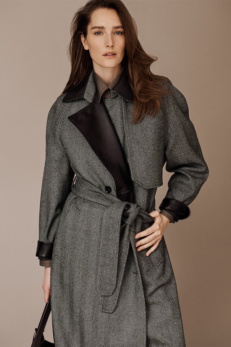 Woman wearing a Brioni gray herringbone coat with black leather collar and cuffs against a beige background