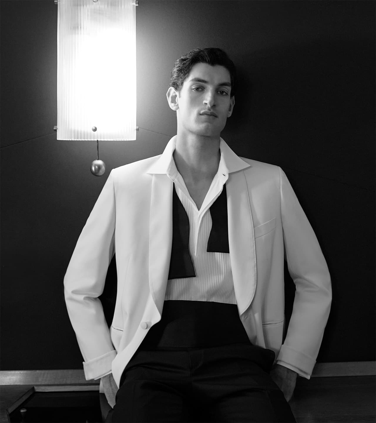Person in white Brioni blazer and striped shirt with black bow tie in dramatic black and white portrait lighting.