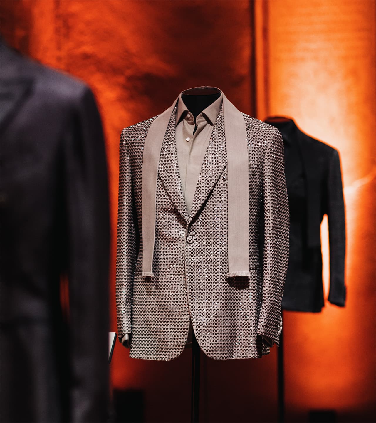 Brioni elegant textured gray suit jacket with matching shirt displayed on mannequin against warm orange backdrop.