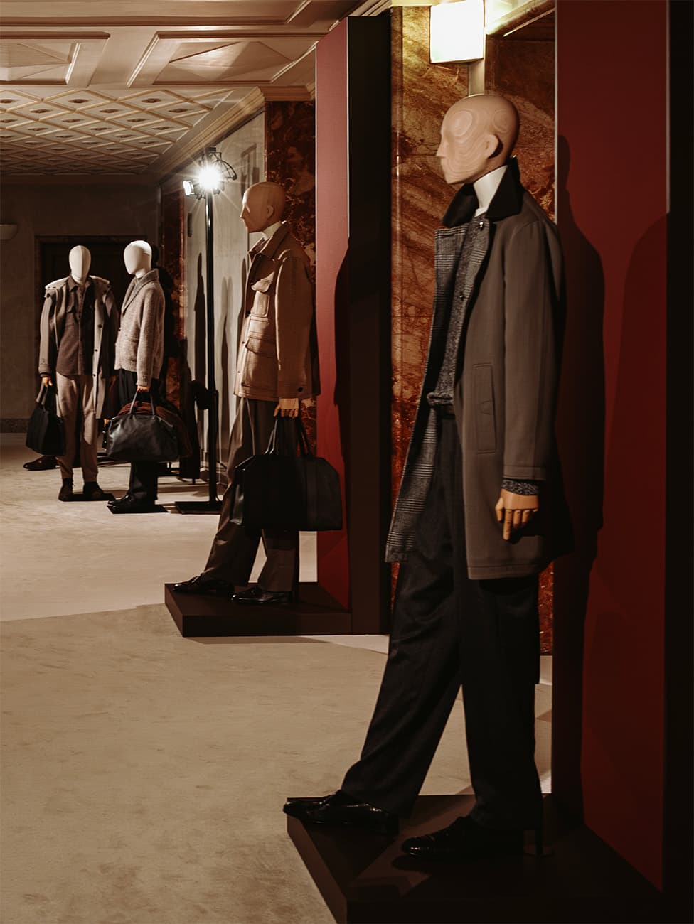 Mannequins displaying men's Brioni formal wear and outerwear in an elegant showroom with marble walls and ornate ceiling.