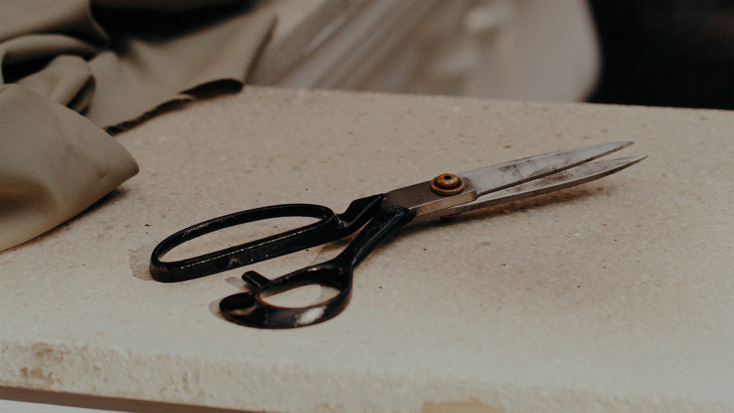 Vintage tailoring scissors with black handles on a beige surface, with fabric material nearby in muted tones.