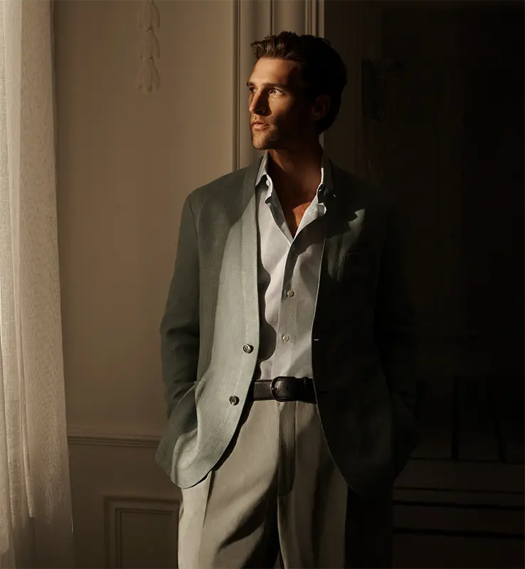 Man in brioni suit with olive jacket and white shirt leaning on wall