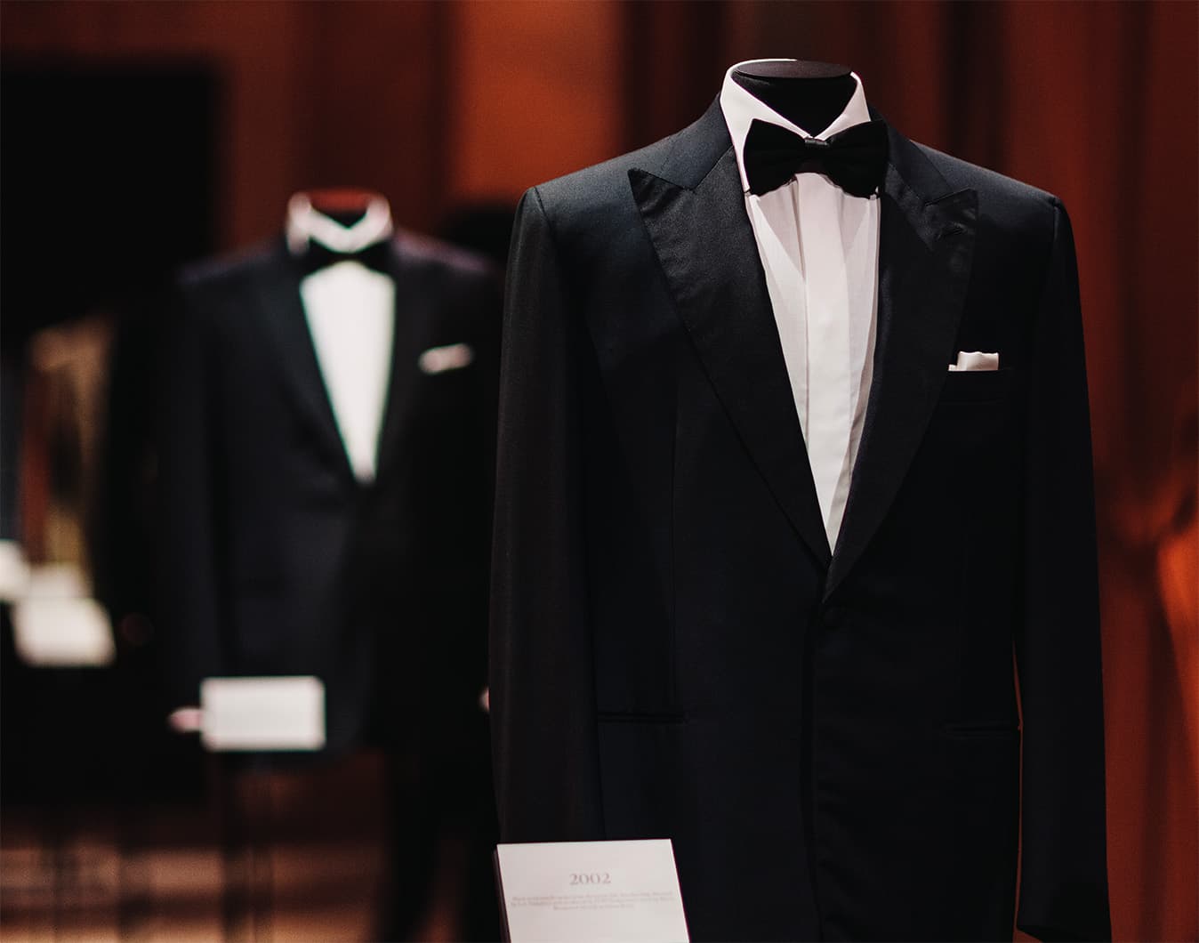 Brioni fashion display featuring elegant tuxedos in white, red, and blue under warm lighting in a historic arched venue.