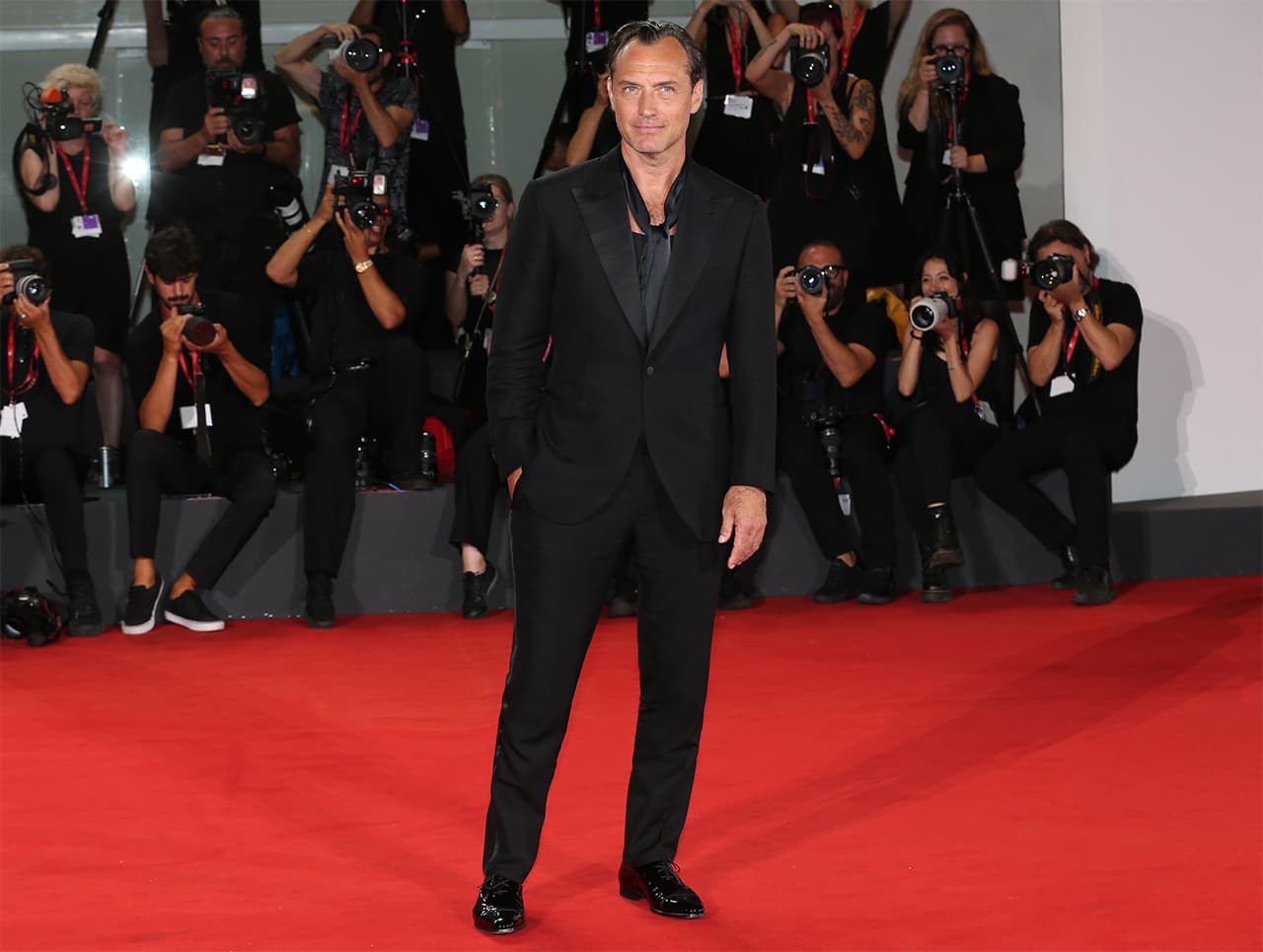 Jude Law in Brioni's black suit standing on red carpet at premiere event with photographers capturing the moment in background.