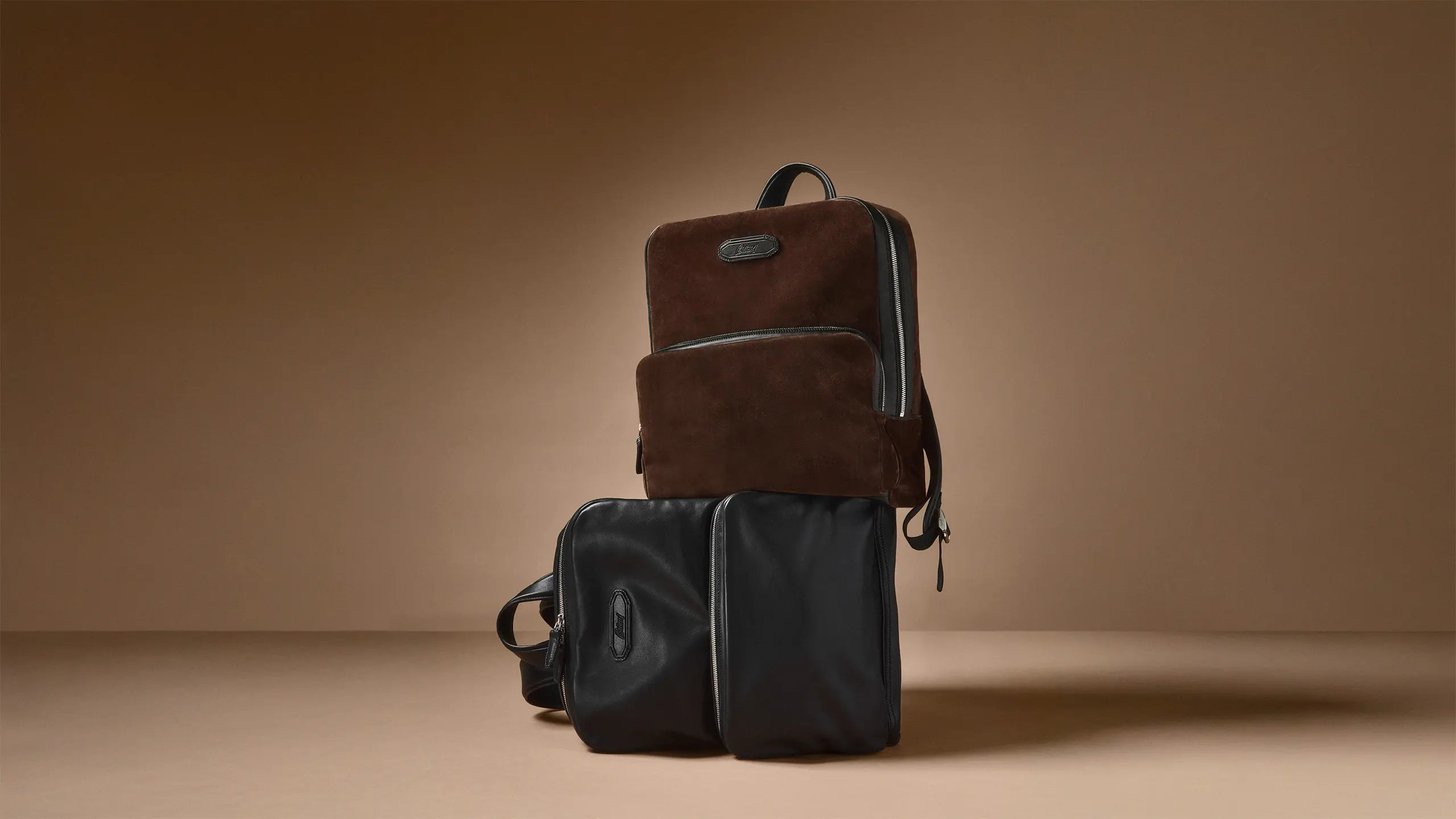 Two Brioni luxury leather travel bags on beige background.