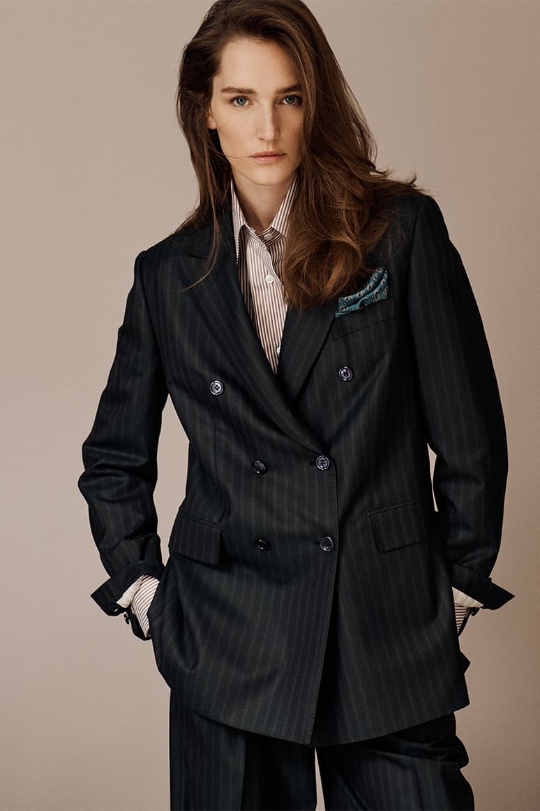 Woman in Brioni dark green pinstriped double-breasted blazer with striped shirt and pocket square against beige background.