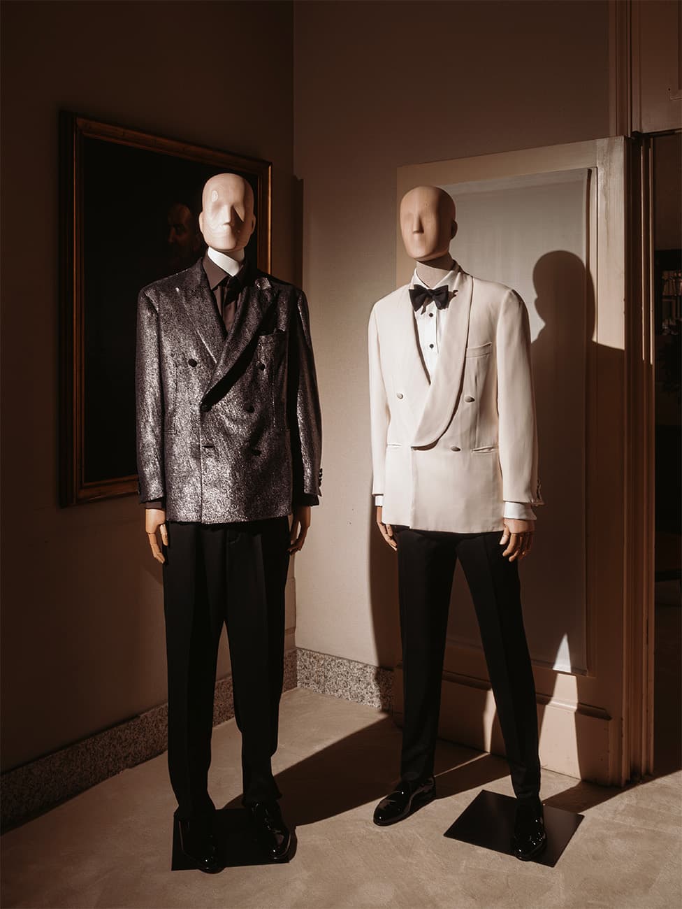 Two mannequins displaying Brioni formal attire - one in a metallic gray jacket and one in a white tuxedo with bow tie.
