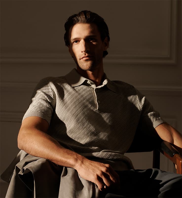 Man in Brioni grey knitwear polo sitting down