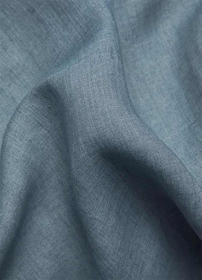 Close-up of Brioni soft blue-gray linen fabric with gentle folds and draping, showing detailed weave texture and natural wrinkles.