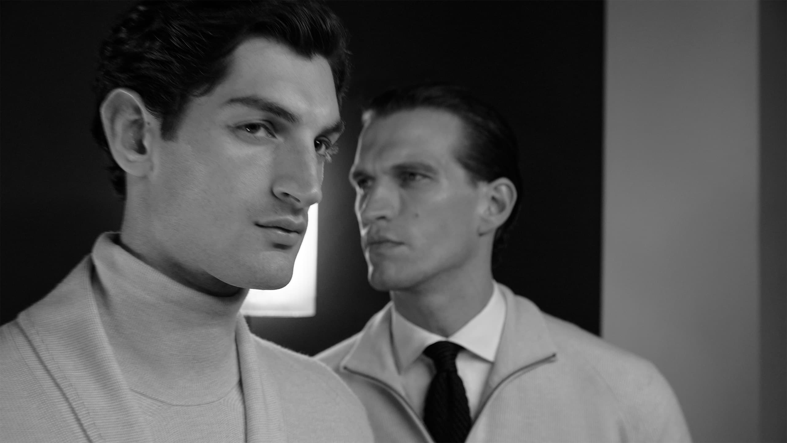 Two men in light-colored Brioni clothing in a black and white portrait, one in a turtleneck and one in a suit with tie.