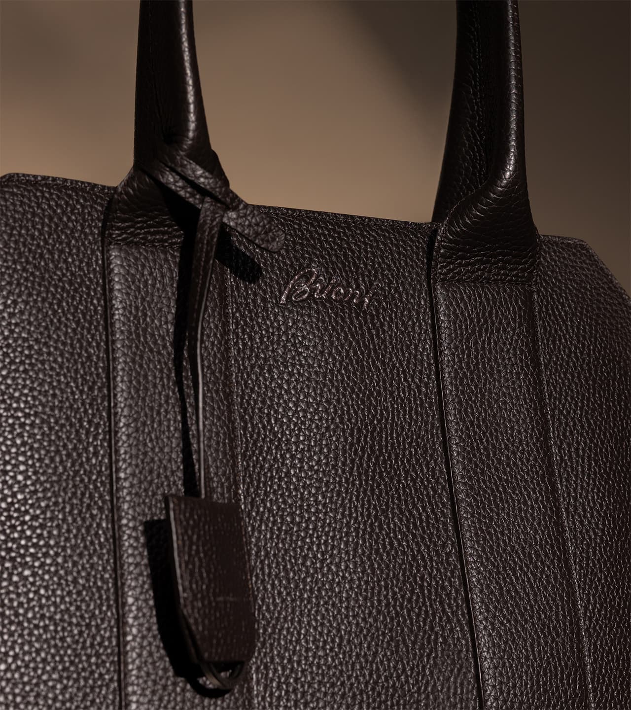Close-up of a Brioni black textured leather Brioni handbag with embossed logo and knotted handles against a neutral background.