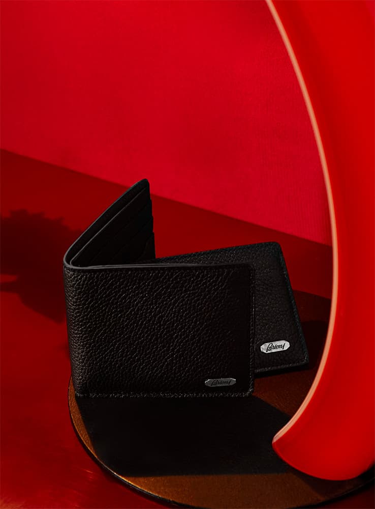 Black leather Brioni wallet displayed against a vibrant red curved background on a dark wooden surface.